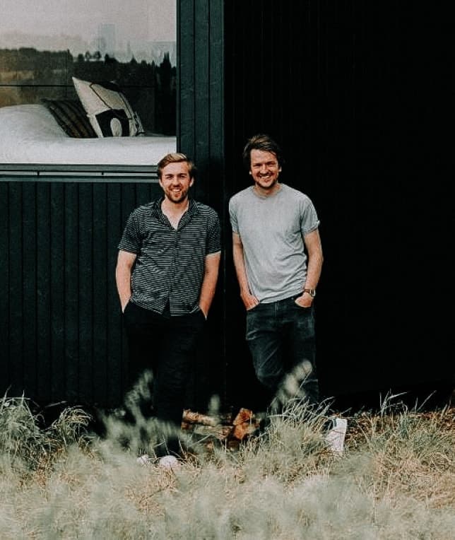 two partners standing agains a wood cabin