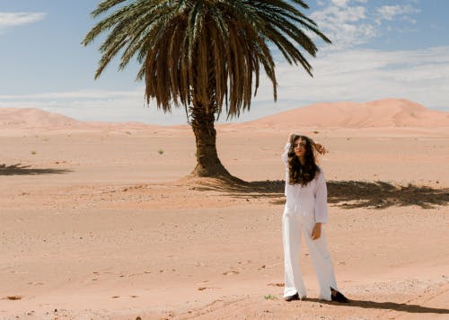 a lady standing in the desert, with palmstrees in the background